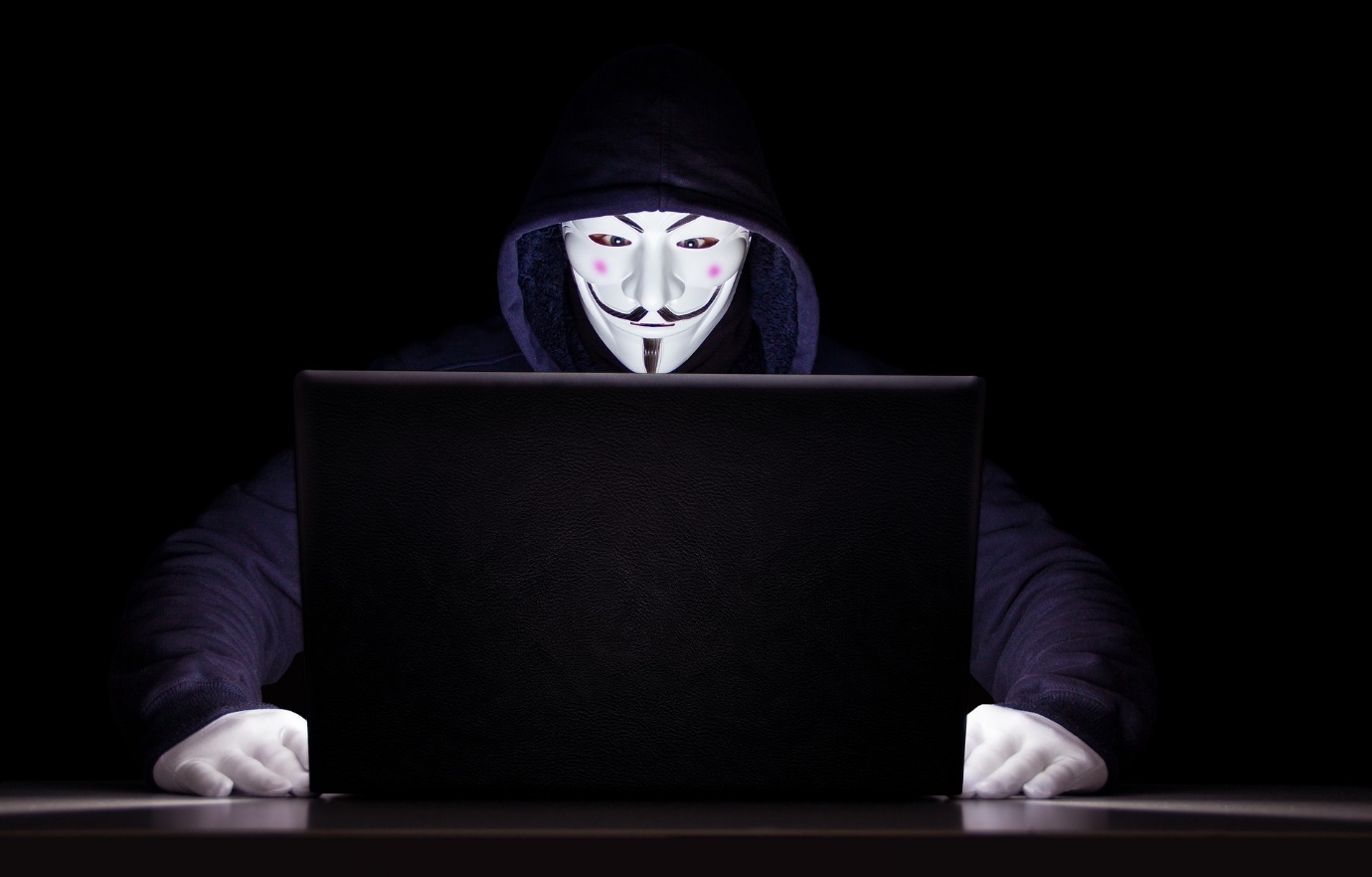 hacker holding white mask looking at laptop computer